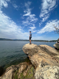 Rear view of man standing on rock by sea against sky