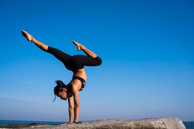 Young woman exercising at beach against clear blue sky