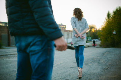 Midsection of criminal standing holding knife while woman with hands tied behind back running on road