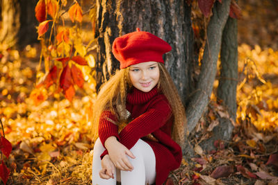 Happy child caucasian girl sitting near a tree in the park on a sunny day