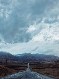 Empty road leading towards mountains against sky