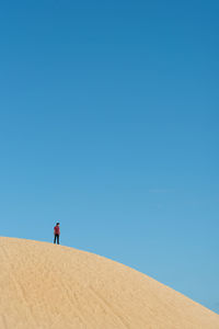 Low angle view of man standing on sand dune against blue sky