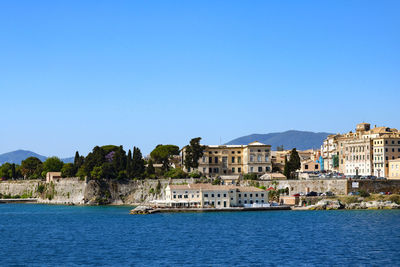 Buildings by sea against clear blue sky