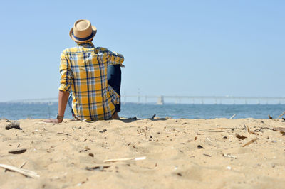 Rear view of man sitting on sand at beach against sky at kent island