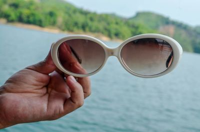 Close-up of hand holding sunglasses against water