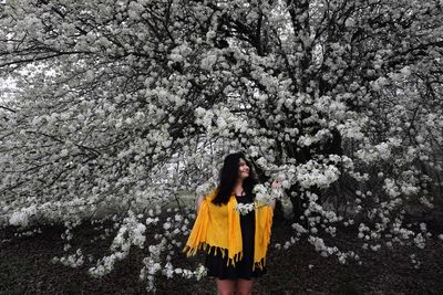 Smiling young woman standing amidst flowering tree branches