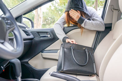 Young woman picking up purse from car