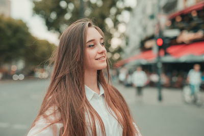 Close-up of smiling young woman standing on street in city