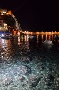 Illuminated city by sea against sky at night