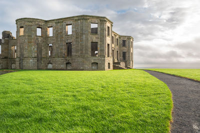 Lawn by building on field against sky