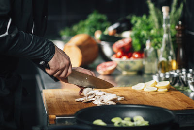 Cooking dinner - chef holding a knife, cutting mushrooms on a wooden cutting board