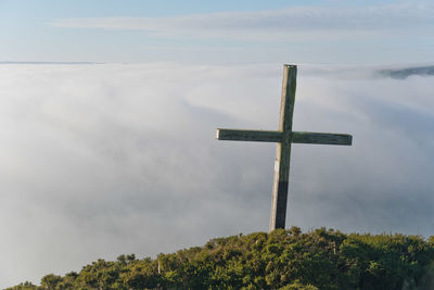 View of wooden cross on a hill looking down at a blanket of fog