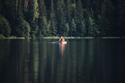 Man rowing boat in lake against trees