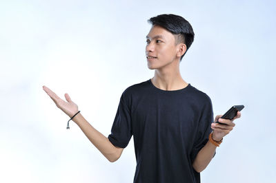 Young asian student man holding a smart phone and open hand palm aside, presenting to copyspace