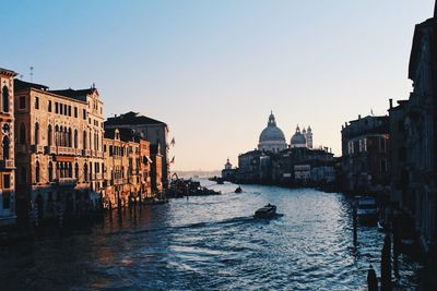 Canal passing through city against clear sky during sunset