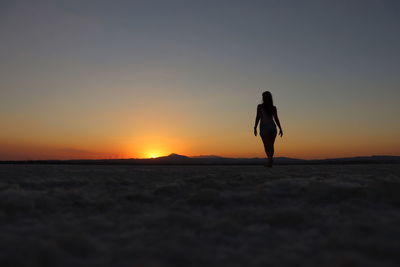 Silhouette woman standing on land against sky during sunset