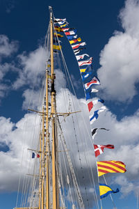 Low angle view of various flags on mast against cloudy sky