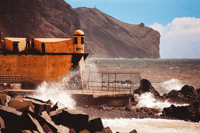 Water splashing on rocks by sea against sky