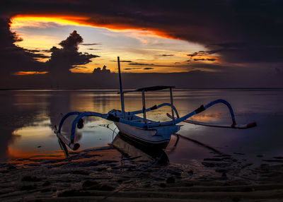 Boat moored on beach against sky during sunset