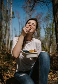 Young woman eating food while sitting in forest