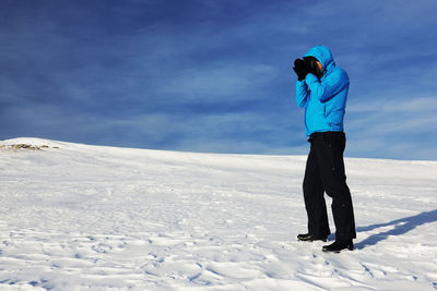 Full length of man photographing with camera on snow covered field against sky