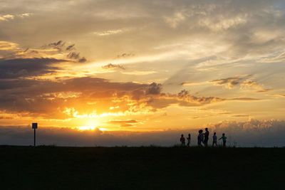 Silhouette people on field against sky during sunset