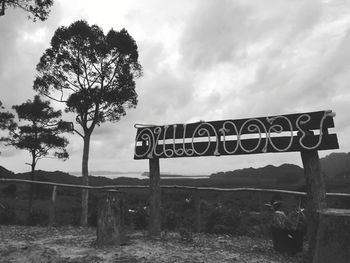 Information sign on road by trees against sky