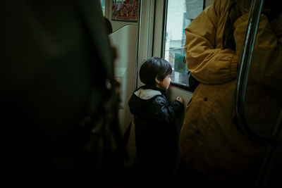 Rear view of boy standing by train window
