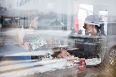 Happy female friends sitting at restaurant seen through window