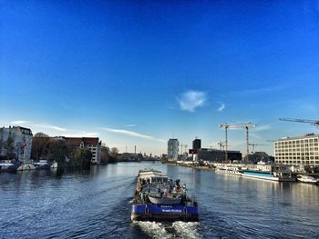 Boats moored on river in city against blue sky