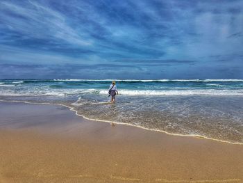 Rear view of woman walking at beach against sky