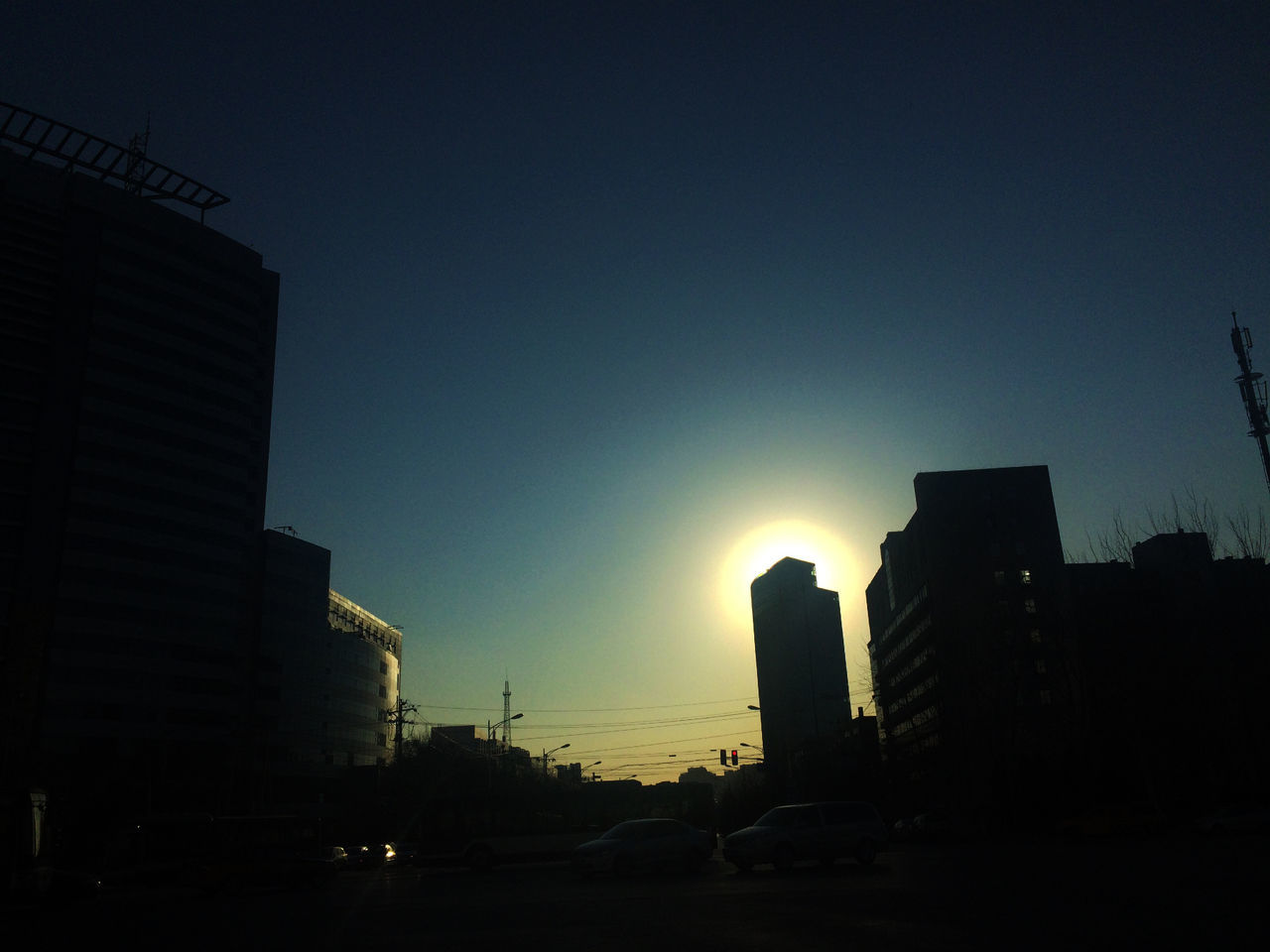 building exterior, architecture, built structure, city, silhouette, clear sky, sunset, copy space, low angle view, building, sun, sunlight, skyscraper, sky, dark, city life, outdoors, tall - high, dusk, development