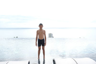 Boy standing at swimming pool with sea view