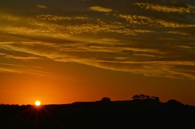 Silhouette hill against cloudy sky during sunset