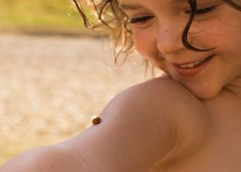 Close-up of cute smiling girl with ladybug on her arm