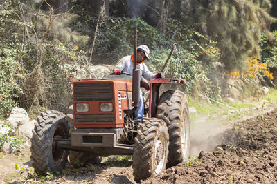 Man driving tractor on dirt road amidst trees in forest