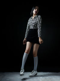 Portrait of a teenage girl standing against black background