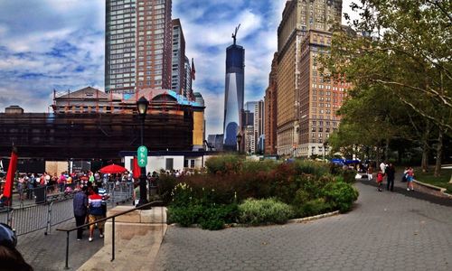 People walking on city street against cloudy sky