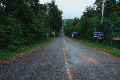 Empty road amidst trees in city against sky