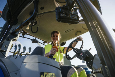 Smiling female farmer holding steering wheel sitting in tractor