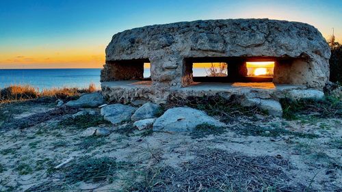 Built structure on rocks by sea against sky during sunset