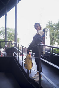 Portrait of smiling businesswoman with backpack standing by railing on footpath