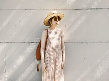 Woman wearing hat standing against white wall