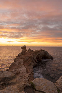 Rocks on beach against sky during sunset