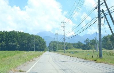 Road by electricity pylon against sky