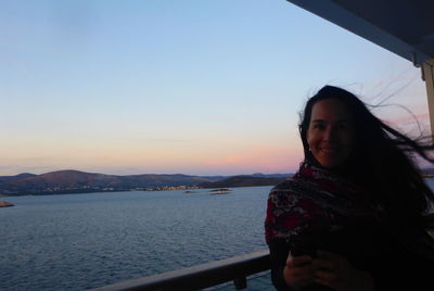 Portrait of smiling woman standing by railing against sky during sunset