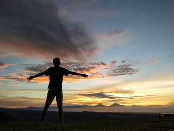 Man with arms outstretched standing at beach against sky during sunset