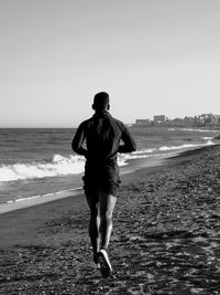 Rear view of man running at beach against clear sky