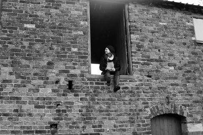 Low angle view of person photographing against brick wall