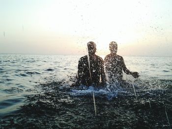 Sea waves splashing on shore against clear sky during sunset